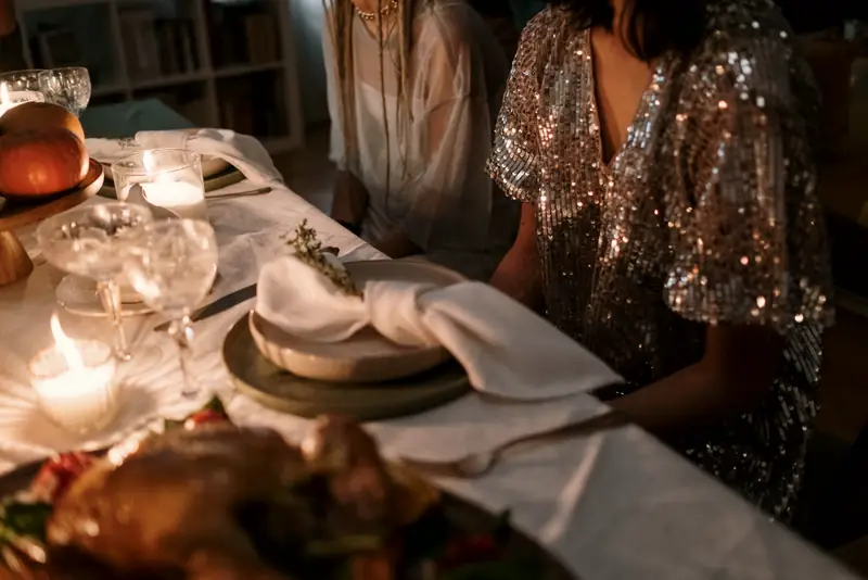 A guest in a sequined dress at a long dinner table set with linen napkins and glowing votives