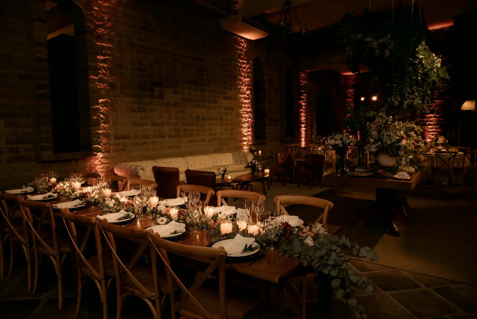 One long candlelit table set for ninety inside a brick warehouse, minutes before the doors open