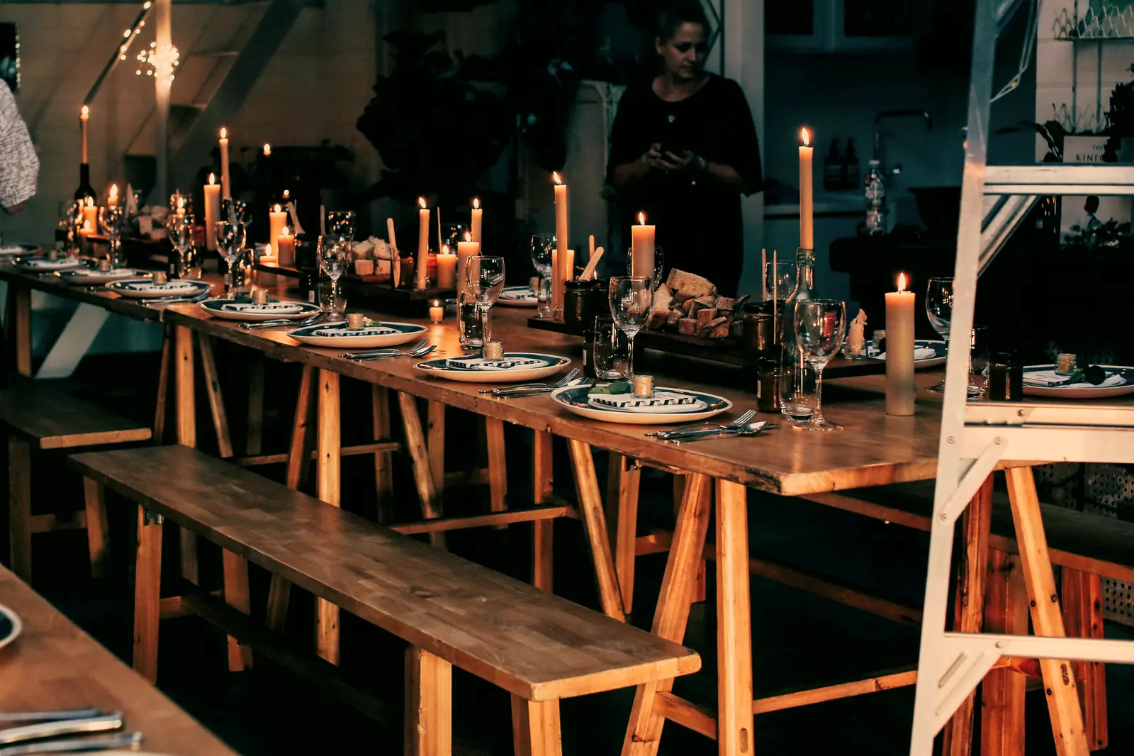 Our crew sets tapers and place settings along a long wooden table in a dim warehouse before guests arrive