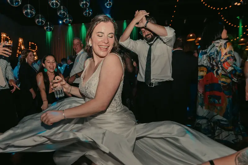 A laughing bride spins on the dance floor while friends hold out the hem of her dress