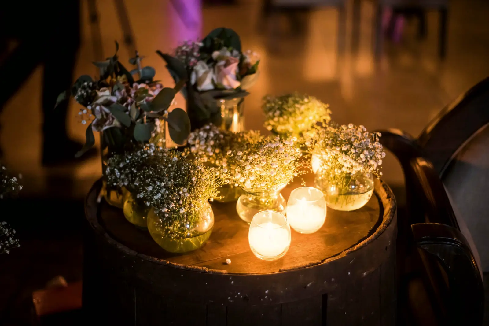Small jars of baby’s breath and dark foliage glowing among votive candles on an old wine barrel